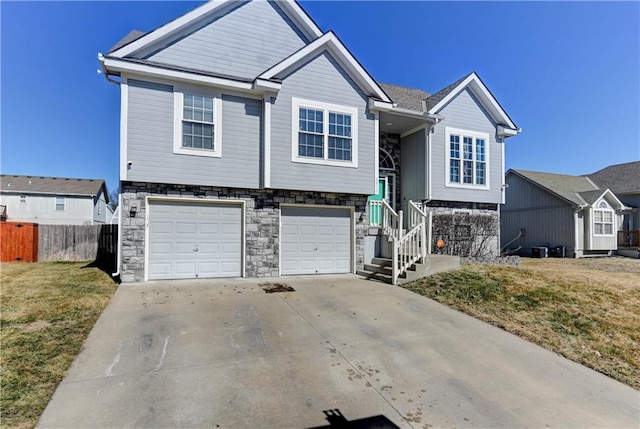 bi-level home featuring an attached garage, fence, stone siding, driveway, and a front lawn