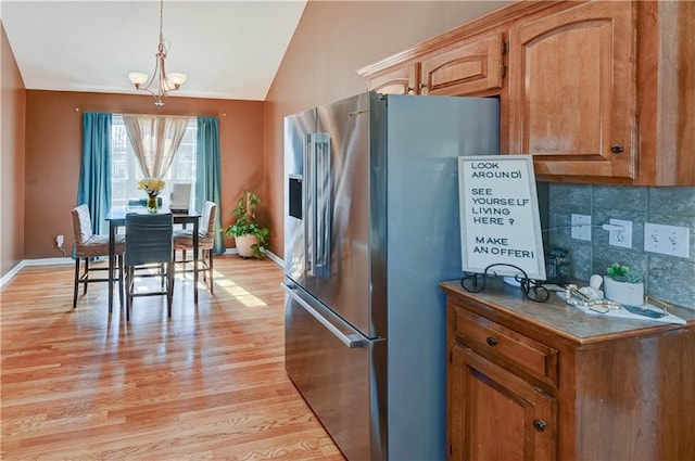 kitchen with lofted ceiling, light wood-style floors, baseboards, stainless steel fridge with ice dispenser, and tasteful backsplash