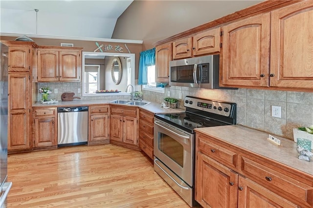 kitchen featuring stainless steel appliances, light countertops, vaulted ceiling, a sink, and light wood-type flooring