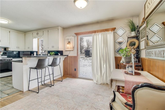 kitchen featuring wainscoting, dark countertops, white cabinetry, and white range with gas stovetop