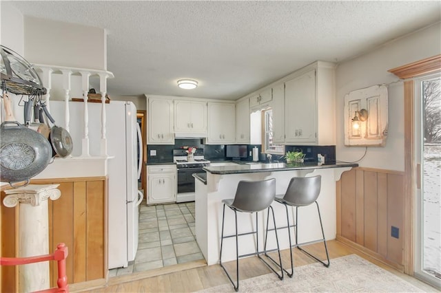 kitchen featuring a peninsula, white appliances, dark countertops, and white cabinetry