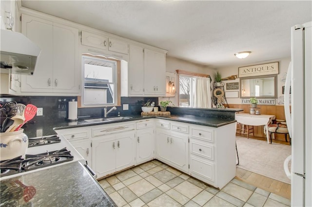 kitchen with dark countertops, white cabinetry, a sink, and freestanding refrigerator