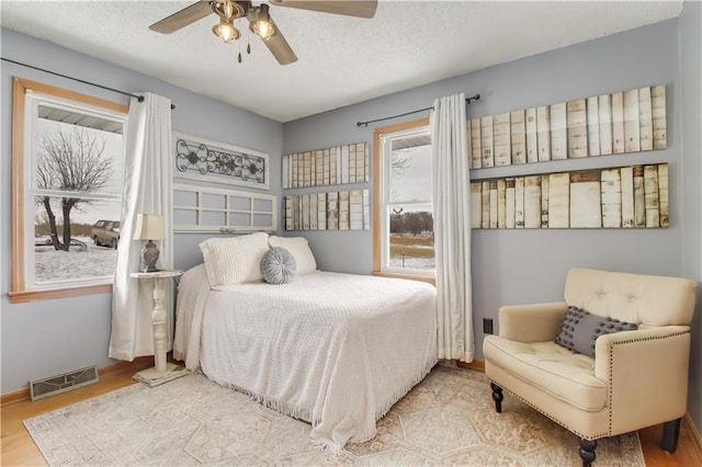 bedroom with a textured ceiling, wood finished floors, a ceiling fan, visible vents, and baseboards