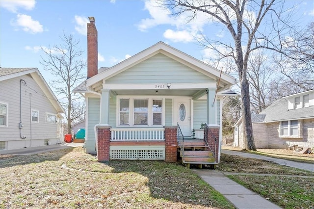 view of front of home with covered porch, a chimney, and a front yard