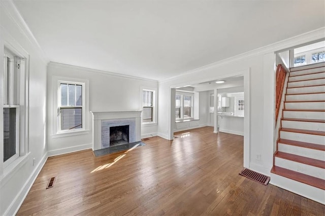 unfurnished living room featuring visible vents, ornamental molding, a brick fireplace, wood finished floors, and stairs