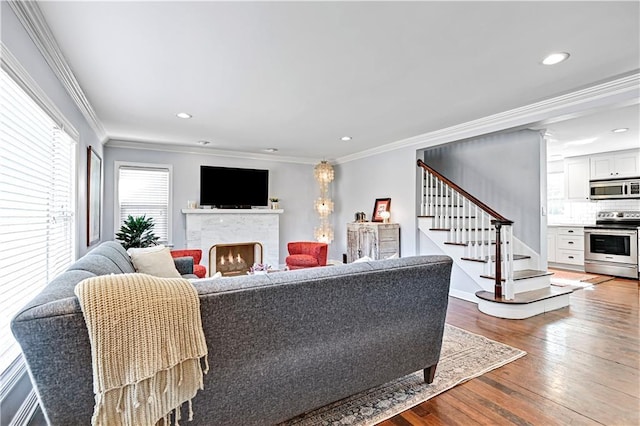 living room with stairs, a lit fireplace, ornamental molding, and wood finished floors