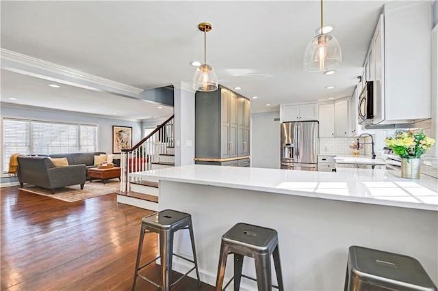 kitchen with a peninsula, open floor plan, light countertops, appliances with stainless steel finishes, and pendant lighting