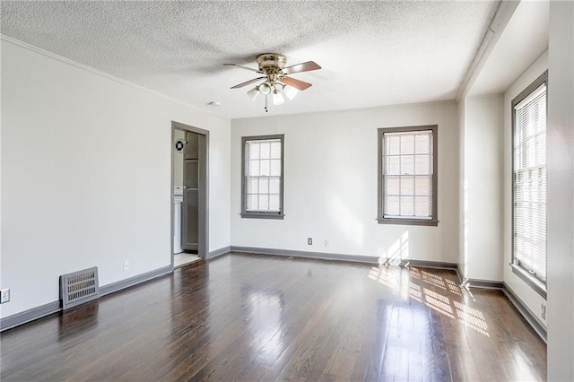 empty room with a healthy amount of sunlight, visible vents, dark wood finished floors, and a textured ceiling