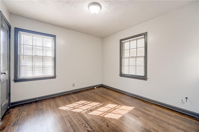 unfurnished room featuring a textured ceiling, baseboards, wood finished floors, and a healthy amount of sunlight