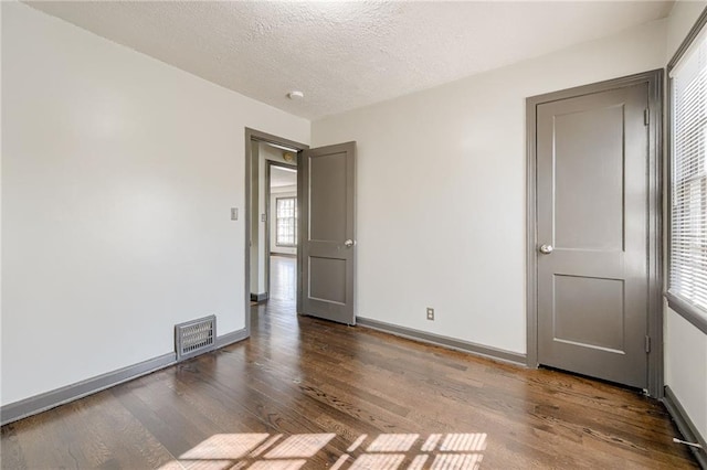 unfurnished room featuring visible vents, a textured ceiling, baseboards, and wood finished floors