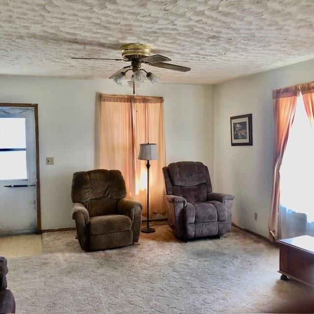 living area featuring a textured ceiling, ceiling fan, carpet, and a healthy amount of sunlight