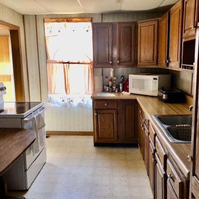 kitchen featuring brown cabinets, light floors, light countertops, a sink, and white appliances