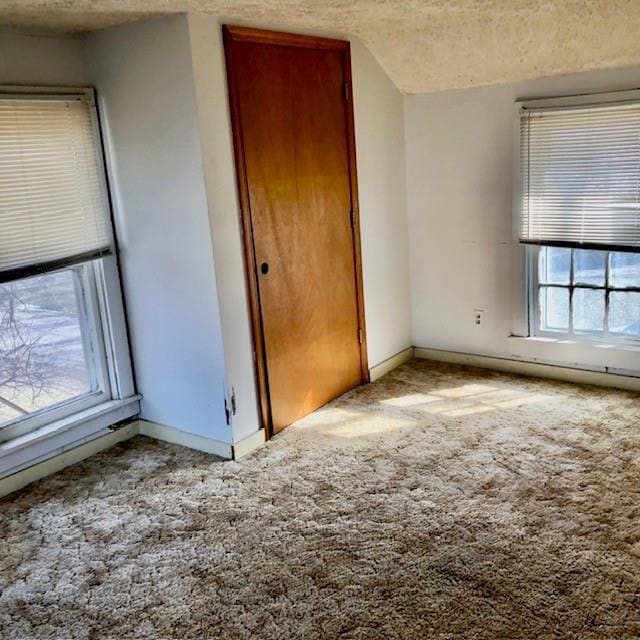 empty room featuring light carpet, a textured ceiling, and baseboards