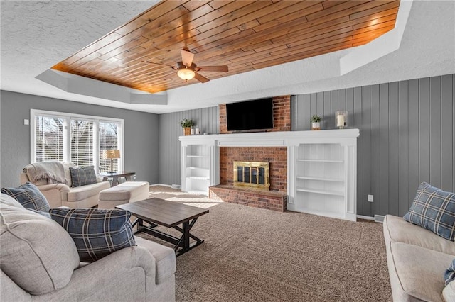 carpeted living area featuring a raised ceiling, built in shelves, wooden ceiling, and ceiling fan