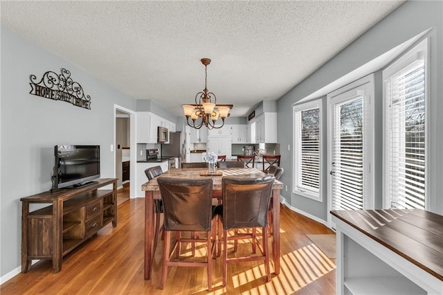 dining area with baseboards, light wood-style floors, a chandelier, and a textured ceiling