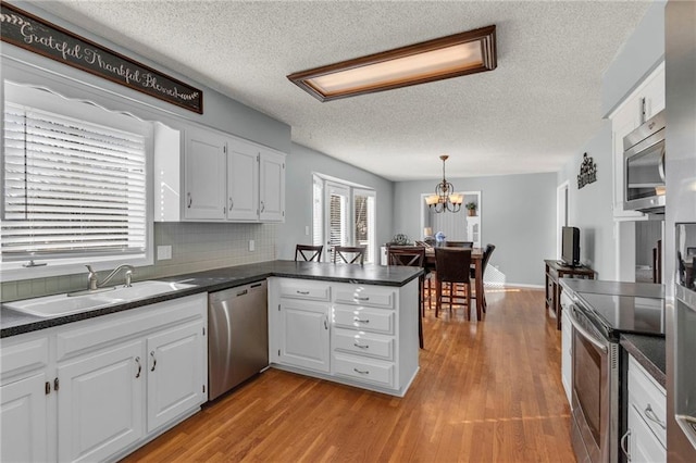 kitchen featuring a peninsula, a sink, white cabinets, appliances with stainless steel finishes, and dark countertops