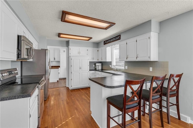 kitchen featuring a sink, stainless steel appliances, dark countertops, and a peninsula