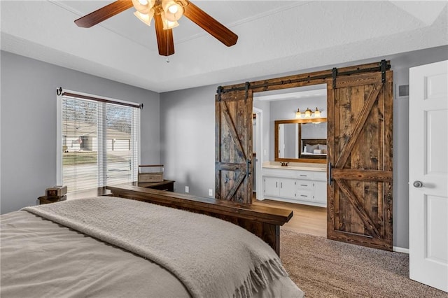 bedroom featuring visible vents, ceiling fan, a barn door, ensuite bath, and a raised ceiling