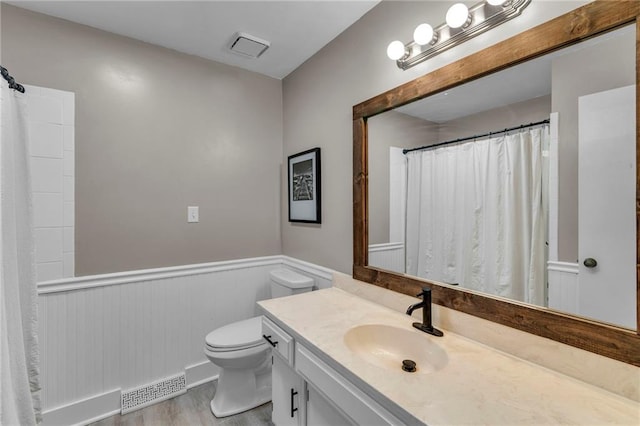 full bathroom featuring vanity, wood finished floors, a wainscoted wall, visible vents, and toilet