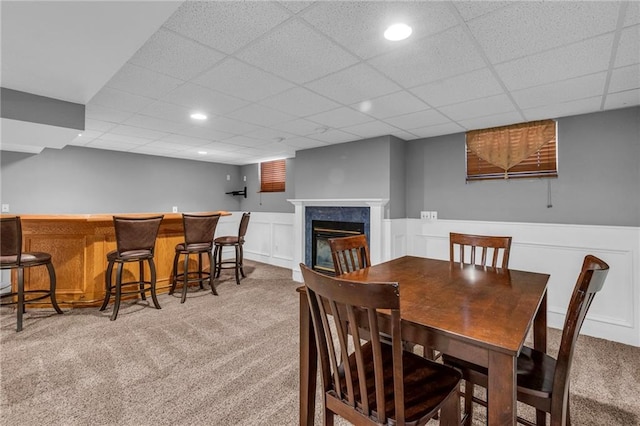 dining room with recessed lighting, a fireplace, a drop ceiling, wainscoting, and light carpet