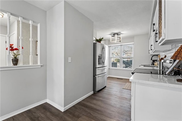 kitchen featuring dark wood-type flooring, stainless steel refrigerator with ice dispenser, a sink, and white cabinetry