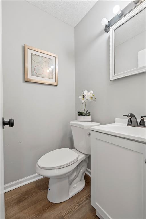 half bath with toilet, a textured ceiling, vanity, wood finished floors, and baseboards