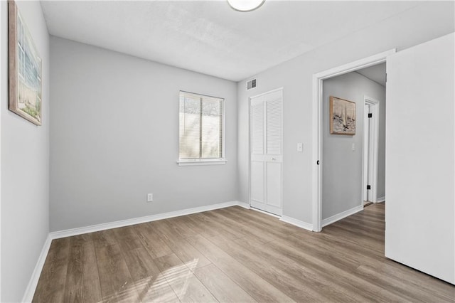 empty room with wood finished floors, visible vents, and baseboards