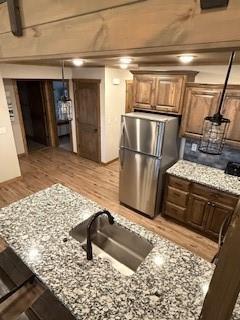 kitchen with light stone countertops, light wood-style floors, a sink, and freestanding refrigerator