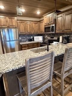 kitchen with appliances with stainless steel finishes, wooden ceiling, a kitchen bar, and decorative light fixtures