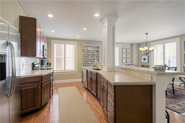 kitchen with light countertops, appliances with stainless steel finishes, hanging light fixtures, an island with sink, and decorative columns