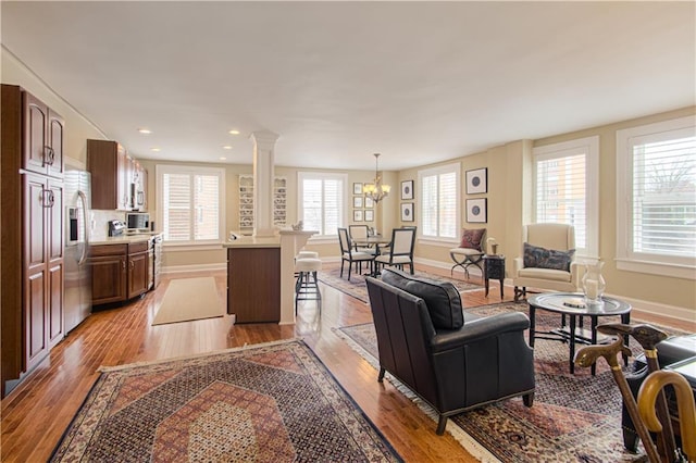 living area with a notable chandelier, recessed lighting, baseboards, light wood-type flooring, and decorative columns