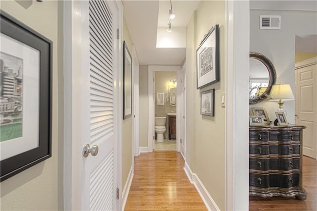 hall with light wood-style flooring, visible vents, and baseboards