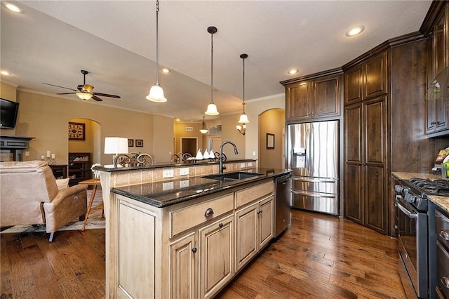 kitchen featuring arched walkways, a sink, open floor plan, appliances with stainless steel finishes, and an island with sink