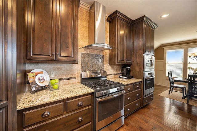 kitchen featuring wall chimney range hood, appliances with stainless steel finishes, backsplash, and dark wood-type flooring