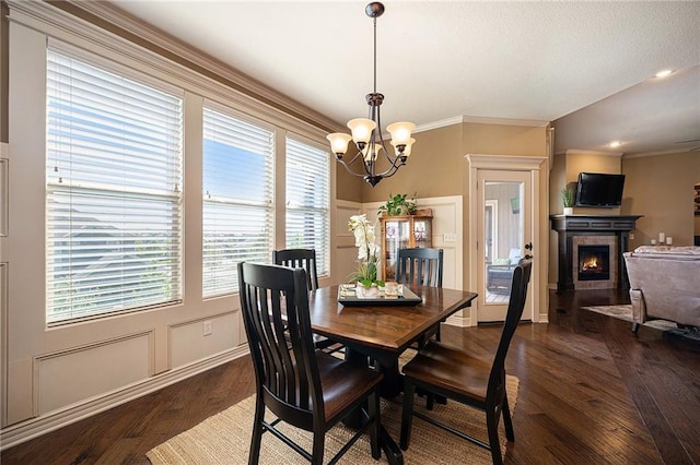 dining space featuring baseboards, dark wood-style floors, crown molding, a fireplace, and a chandelier