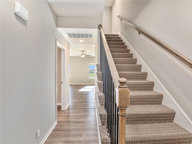 staircase featuring ceiling fan, wood finished floors, visible vents, and baseboards