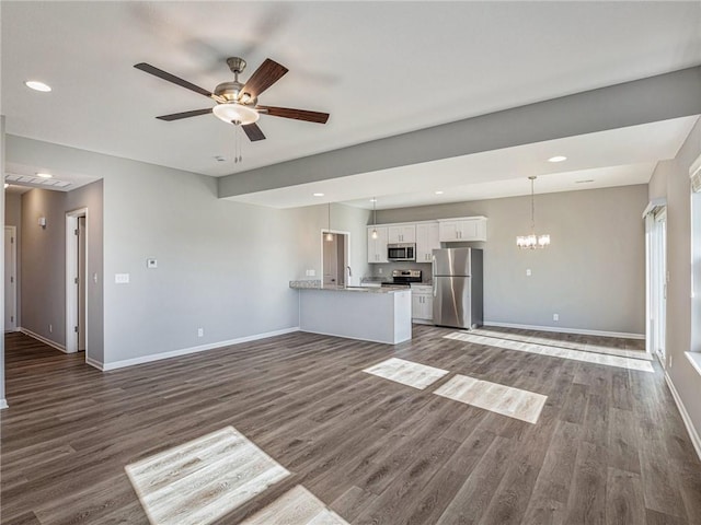 unfurnished living room with ceiling fan with notable chandelier, recessed lighting, dark wood finished floors, and baseboards