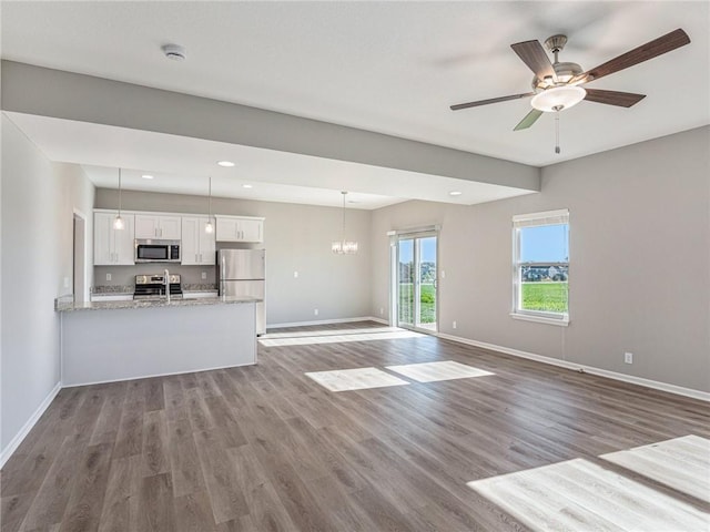 unfurnished living room with ceiling fan with notable chandelier, recessed lighting, baseboards, and wood finished floors