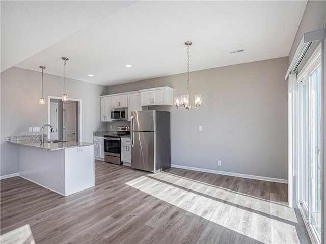 kitchen with white cabinets, light stone counters, appliances with stainless steel finishes, a peninsula, and a sink