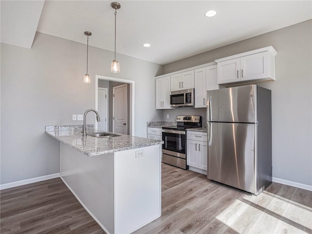 kitchen with a peninsula, white cabinetry, appliances with stainless steel finishes, and decorative light fixtures