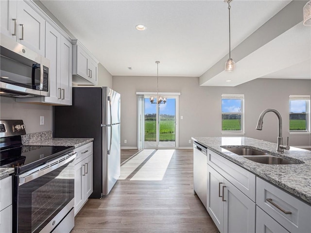 kitchen with a sink, appliances with stainless steel finishes, a wealth of natural light, light stone countertops, and decorative light fixtures