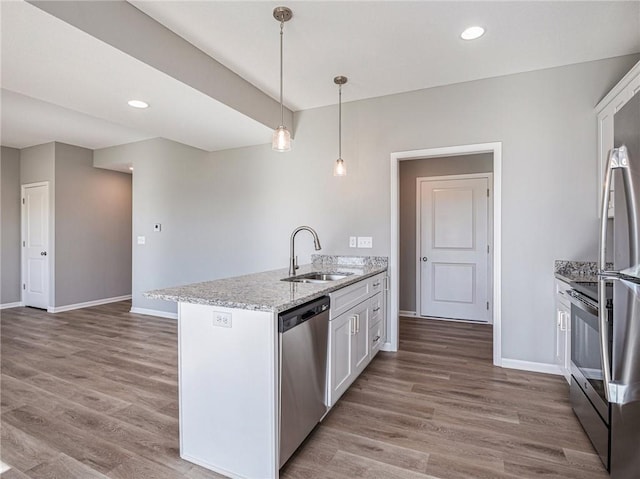 kitchen with light stone counters, a sink, white cabinetry, hanging light fixtures, and appliances with stainless steel finishes