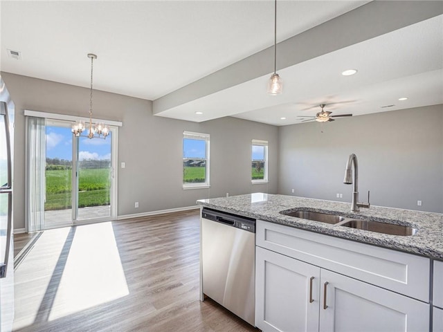 kitchen with white cabinets, open floor plan, light stone countertops, stainless steel dishwasher, and a sink