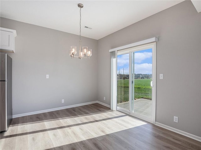 unfurnished dining area with visible vents, a notable chandelier, baseboards, and wood finished floors