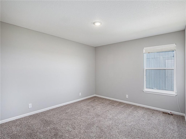 spare room with carpet flooring, a textured ceiling, and baseboards