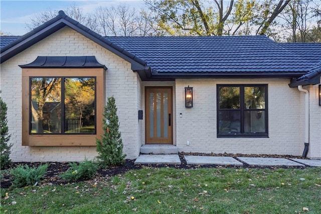 view of front of property featuring brick siding, metal roof, a tiled roof, and a front lawn