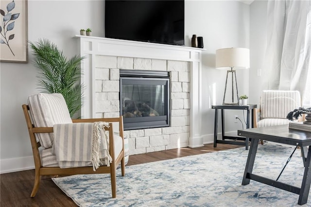 living area with a stone fireplace, wood finished floors, and baseboards