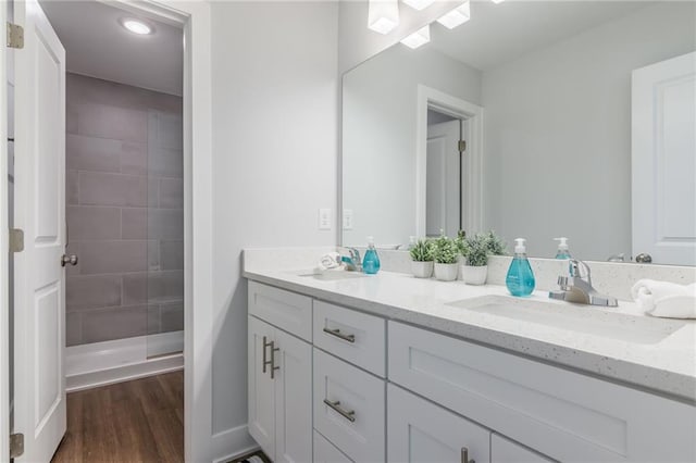 full bath featuring double vanity, tiled shower, wood finished floors, and a sink