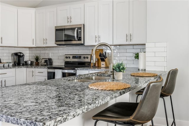 kitchen with light stone countertops, a sink, appliances with stainless steel finishes, white cabinetry, and a kitchen breakfast bar