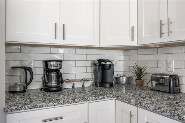 interior details featuring dark stone counters, a toaster, backsplash, and white cabinetry